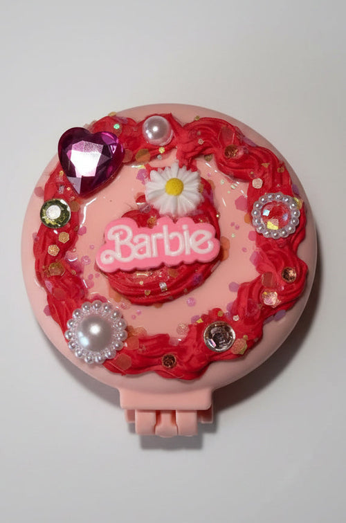 A pink Barbie-themed compact case decorated with red roses, faux pearls, rhinestones, and a small daisy, featuring the Barbie logo on the front, set against a plain light gray background.